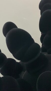 abstract black sculpture made of smooth rounded forms rises against a pale gallery wall, creating a minimalist contemporary art scene with bold shadows and texture