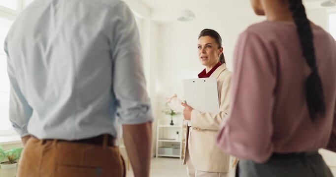Agent and couple consultation during apartment viewing. She explains rental terms on a clipboard, outlining the contract during meeting. Real estate rental discussion and agreement today.