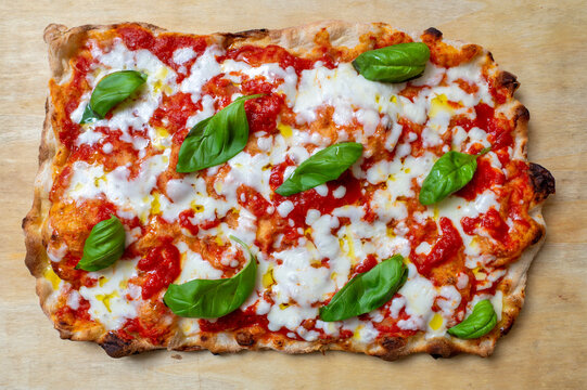 Traditional Roman-style Margherita pinsa topped with tomato sauce, melted mozzarella, fresh basil and extra virgin olive oil, photographed from above on a rustic wooden background
