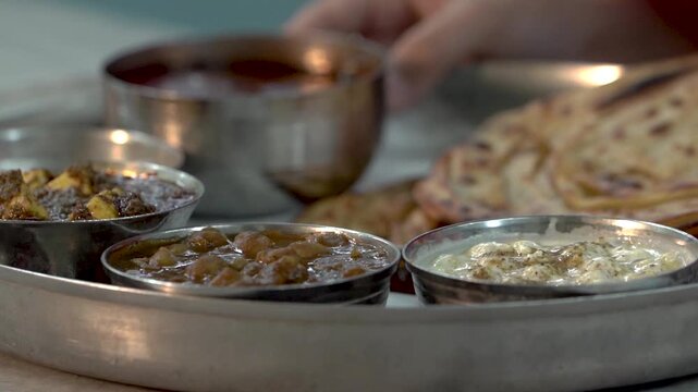 Close up shot of serving authentic Amritsari Punjabi thali with chole, dal tadka, paneer, raita, pickle and freshly made laccha paratha.