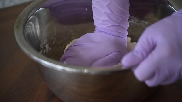 Hands in Purple Gloves Kneading Dough in Stainless Steel Bowl, slow motion
