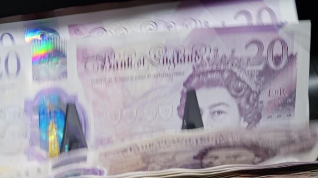 British 20 GBP banknotes rapidly counted by an automatic money counter. Business investment, wealth management, financial growth and capital planning concept.