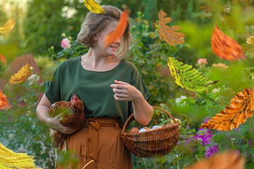 Female farmer gently holds red hen beside chicken coop with basket filled with fresh eggs. Rural lifestyle and responsible poultry care emphasize organic farming © lesichkadesign