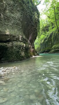 a kayak moves through clear turquoise water between towering mossy limestone cliffs, revealing a quiet forest canyon and adventurous river journey through untouched nature