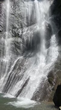 rushing white waterfall spills over dark sculpted rocks into a clear pool, revealing sparkling spray, wet textures and powerful freshwater movement in a wild forest