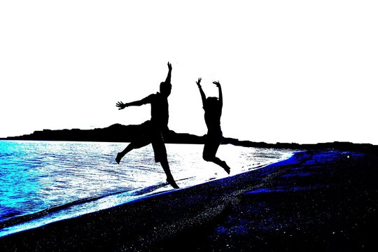 silhouette of a man and lady jumping in the sand beach