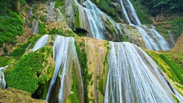 Wide angle view of waterfall cascading down lush green rocky cliffs, Guizhou, China. Perfect for nature and travel concept.