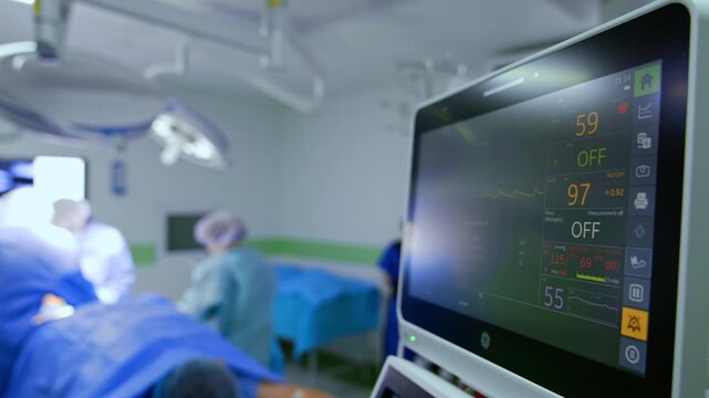 Lung ventilating machine screen with life signs. Close up. Medical team in the blurred backdrop.