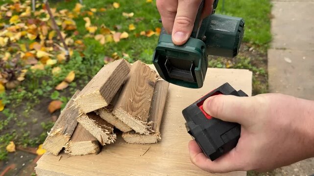 Hands use a cordless power tool to cut small wood pieces on a workbench, outdoor yard setting with autumn leaves, practical diy and home improvement mood