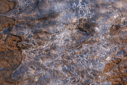 Melting ice sheet on textured rock with winter light