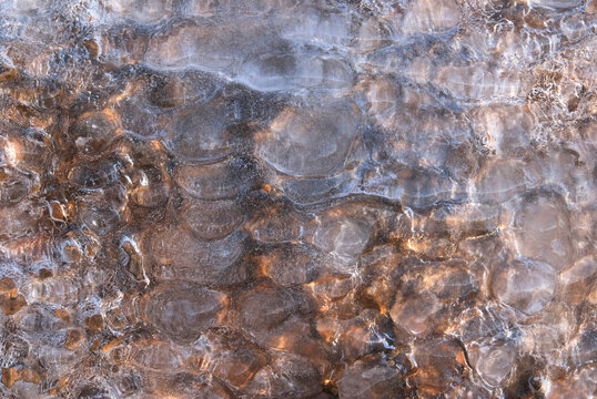 Frozen river surface with smooth ice bubbles and stones