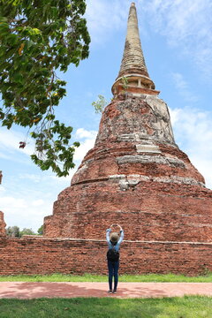 Asian female tourist visits  and use mobile phone to take pictures the old pagoda. Aancient brick structure with bright blue sky, green trees. Main pagoda of Wat Mahathat, Ayutthaya Historical Park.

