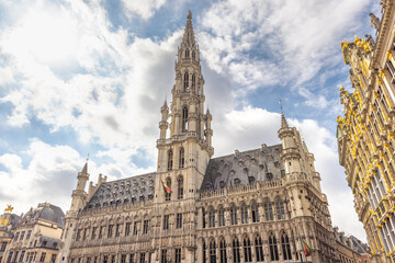 Fototapeta premium City of Brussels in Belgium, Europe. The Town Hall in Grand Place Square, historic European architecture under a bright blue sky with white clouds, showcasing intricate details and classic design