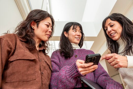 Japanese friends sharing smartphone update in modern hallway
