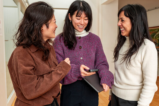 Japanese friends sharing smartphone update in modern hallway