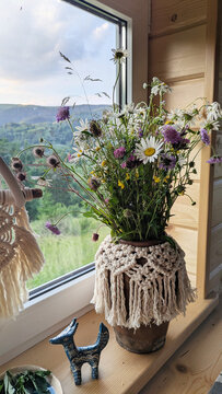 A vase with a bouquet of wildflowers and daisies on a windowsill