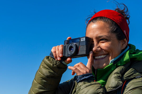 Smiling woman taking a photo with compact camera outdoors