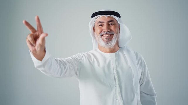 Cheerful senior arab man with a gray beard wearing a shemagh and agal looking at the camera and smiling, expressing happiness and confidence on a clean white background in a studio setting