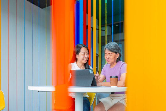Asian mother and daughter using tablet at colorful cafe