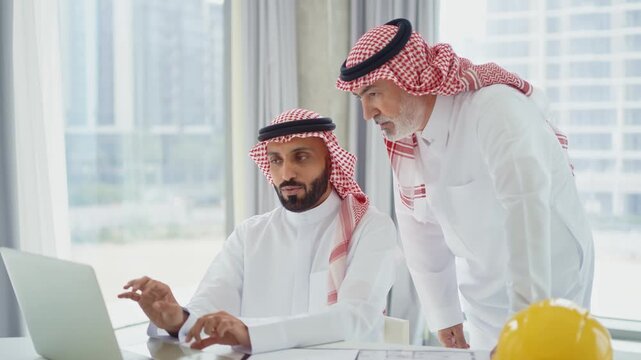 Saudi businessmen collaborating on a laptop in corporate office	