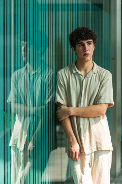 Young man leaning by glass wall with thoughtful mood