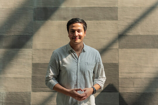 Smiling man standing by stone wall in soft shadow light