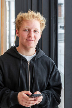 Student taking a break by window with smartphone indoors