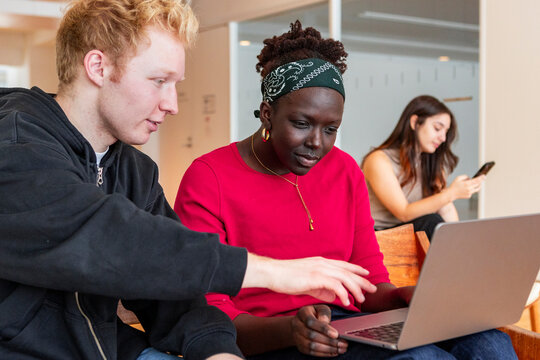 Multiethnic student uses laptop while peer checks phone
