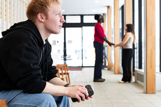Student sitting alone while classmates talk in hallway