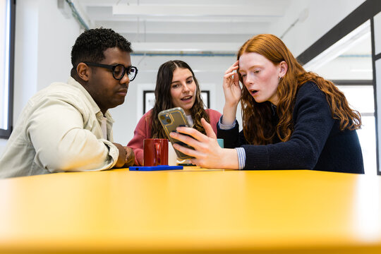 Young coworkers reviewing smartphone data in modern office