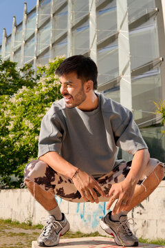 Fashionable urban Hispanic man squatting by modern building