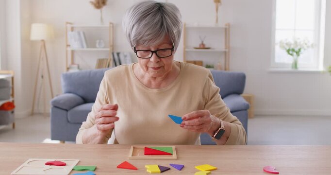 Senior old mature grandmother playing wooden game at home alone, senior grandparent playing wooden boardgame, anti alzheimer activity to improve learning and memory, prevent dementia in older adults