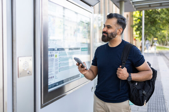 Indian commuter checking timetable with smartphone at station