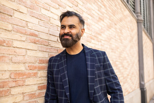 Indian businessman smiling outdoors by brick wall