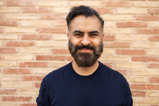Indian man smiling in front of brick wall outdoors