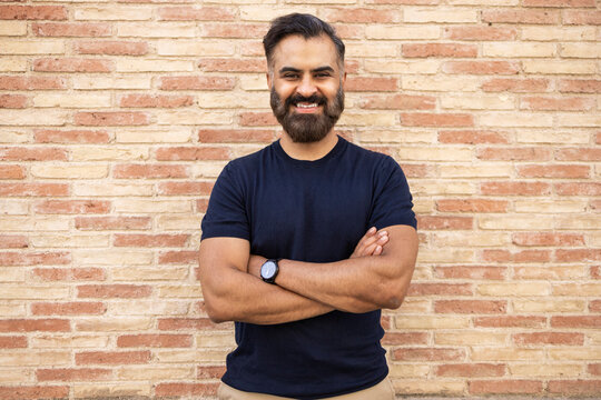 Smiling Indian man with folded arms standing by brick wall