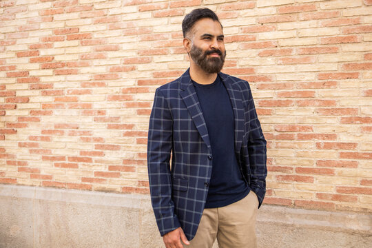 Indian businessman in check blazer standing by brick wall
