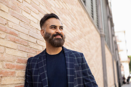 Indian man in checked blazer outdoors by brick wall