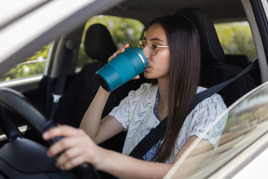 Woman drinking coffee while driving car with seatbelt