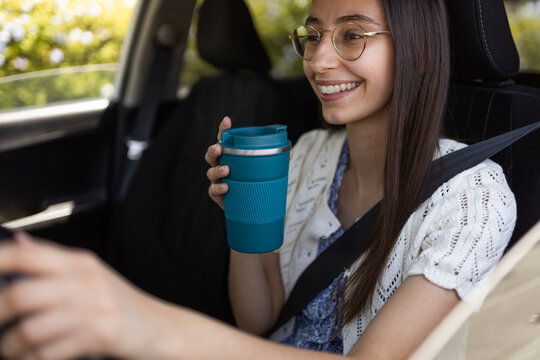 Smiling young woman driving car with reusable coffee cup