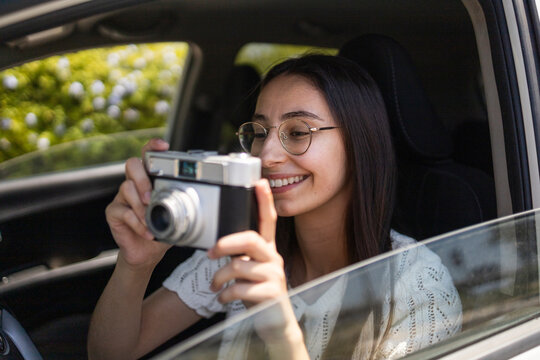 Smiling traveler taking photo with vintage camera in car
