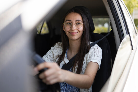 Smiling woman driving car with seatbelt on sunny day