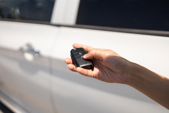 Hand holding car key fob unlocking white vehicle door