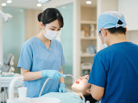 治療中の患者の口元にバキュームを当てて歯科医をアシストする女性