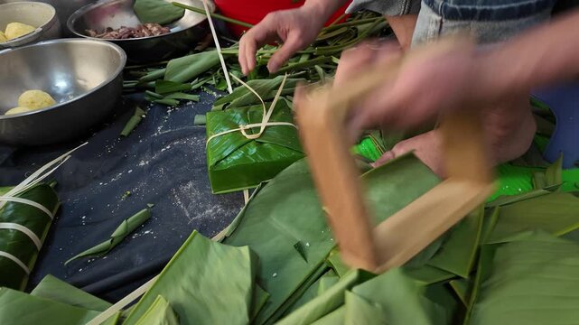 Close up hand making chung cake for Tet holiday at home, Vietnamese lunar new year, traditional food from sticky rice, mung beans, meat wrapping by green dong leaves, bamboo strings