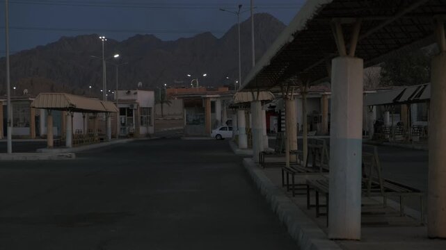 Empty desert bus station before sunrise with mountains and soft blue dawn light creating liminal space atmosphere, quiet urban landscape, solitude, cinematic travel background