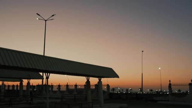Empty desert bus station before sunrise with blinking street light and mountain backdrop creating liminal space atmosphere, quiet cinematic scene of anticipation and isolation