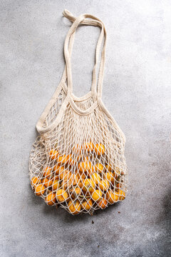 Loquat fruit in reusable mesh bag on gray concrete background