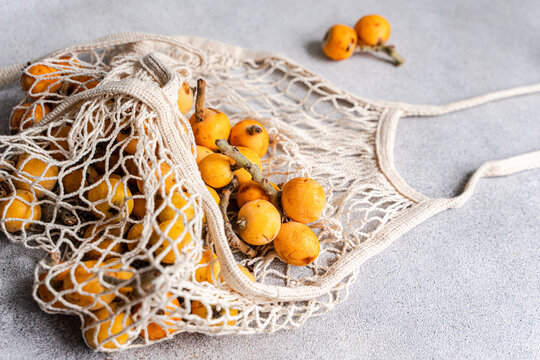Fresh loquat fruit in reusable net bag on gray table