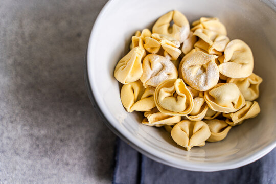 Fresh tortellini pasta in white bowl on gray surface